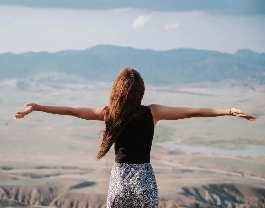 Close-up. A young female tourist stands with her hands up on the top. The girl greets the sun.